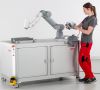 Frau in Arbeitskleidung steuert per Tablet Roboterarm auf fahrbarem Untergestell